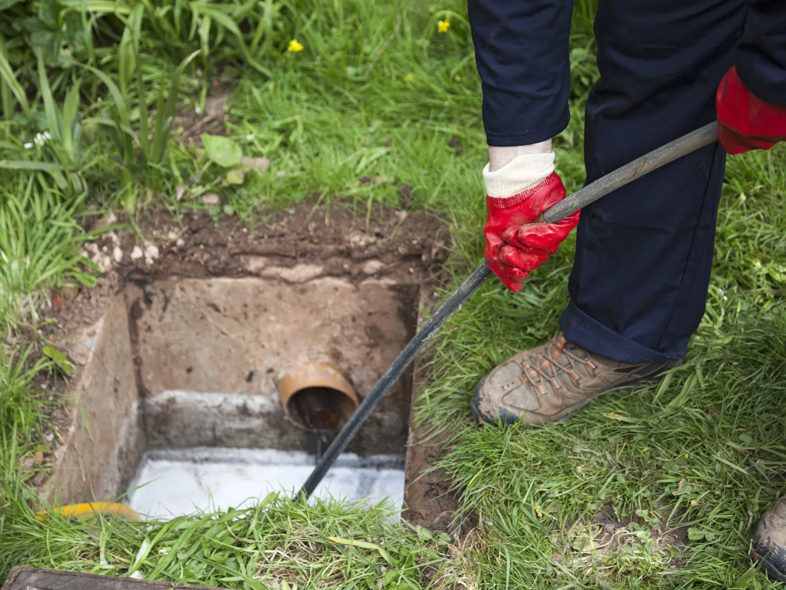 Plumber feeding a drain cleaning cable into an outdoor drain pit to clear a clogged line