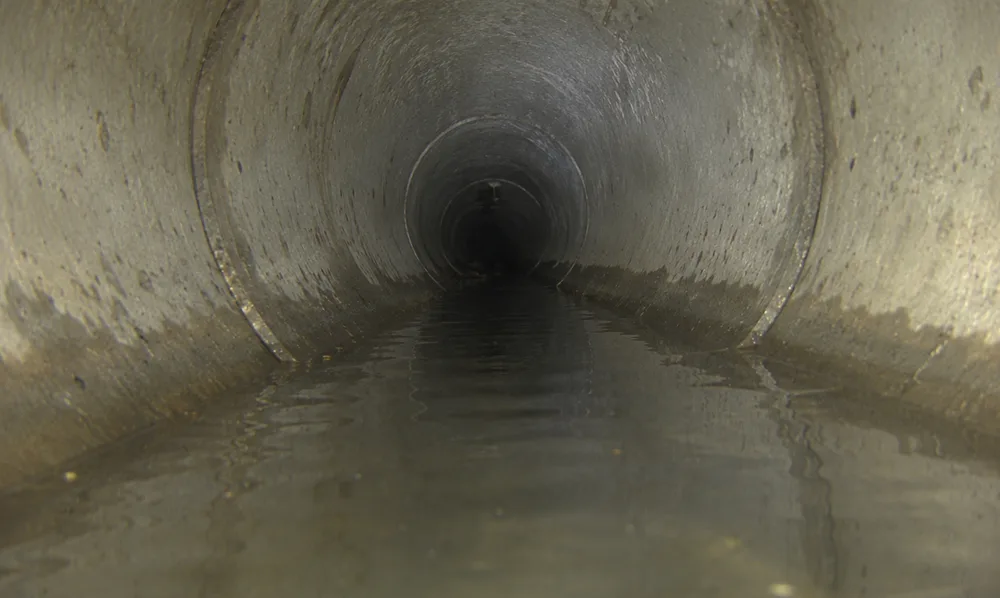 In-pipe camera view down a sewer line showing standing water pooled in a low spot, or belly, in the pipe